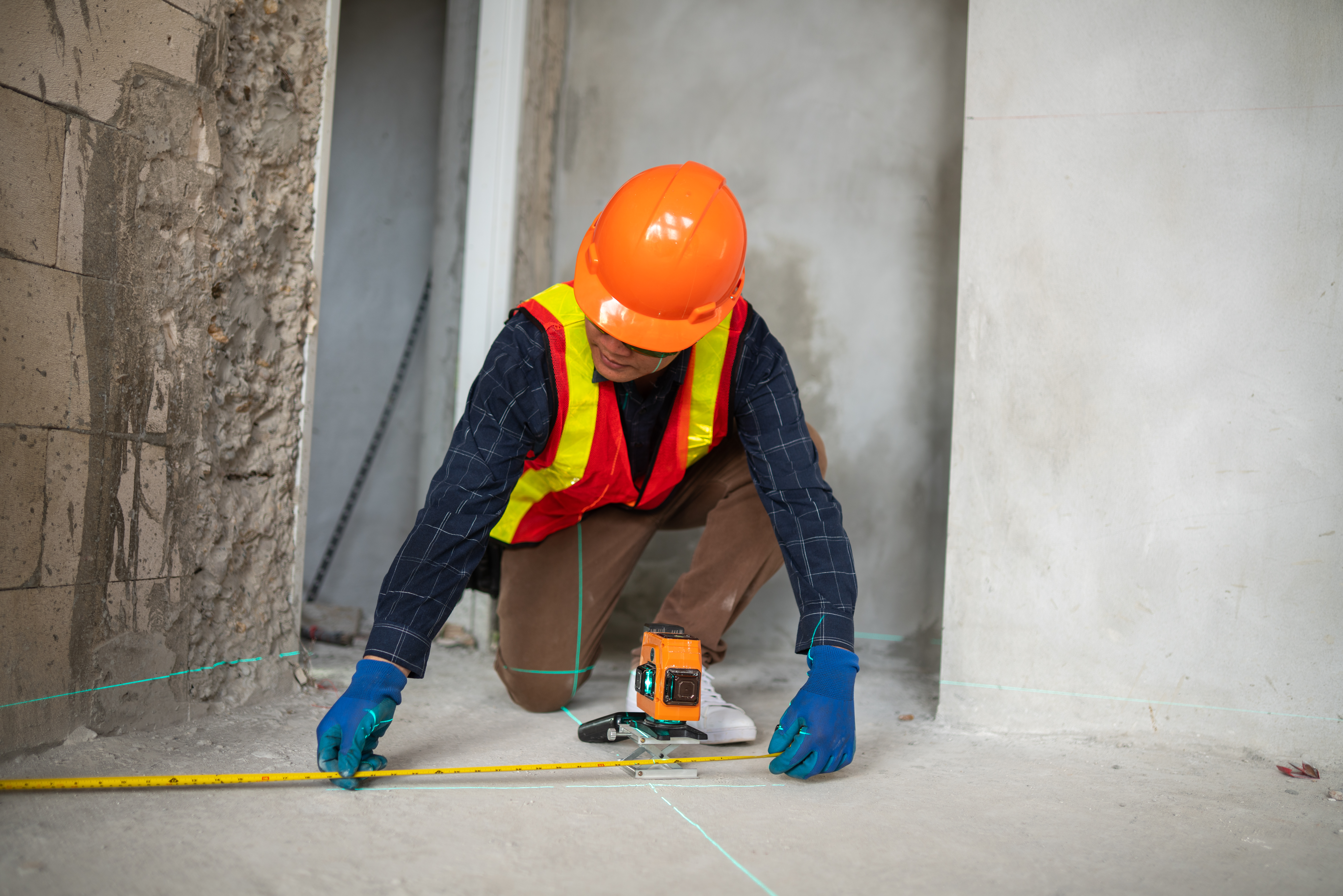 A construction worker uses a laser level to measure the floor in a building under renovation showcasing technical skills in the industry.